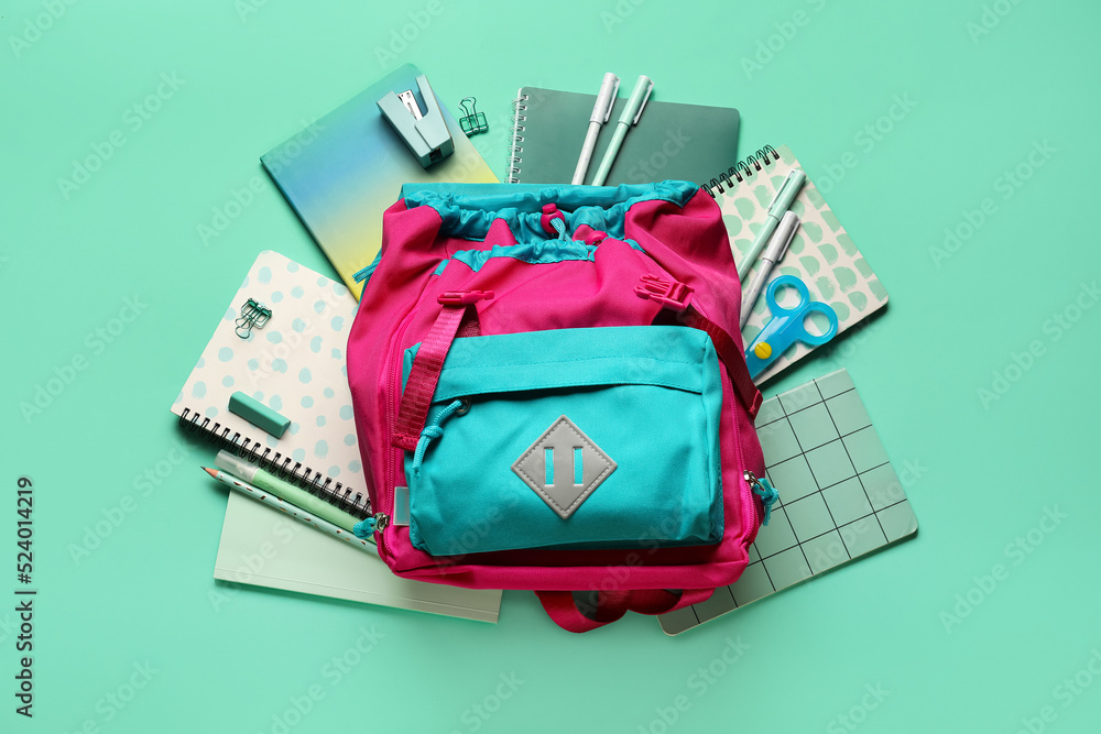 School backpack with stationery on green background