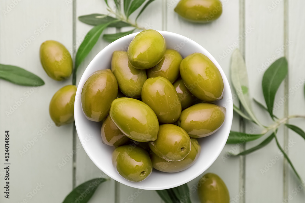 Bowl of green olives on light wooden background, closeup