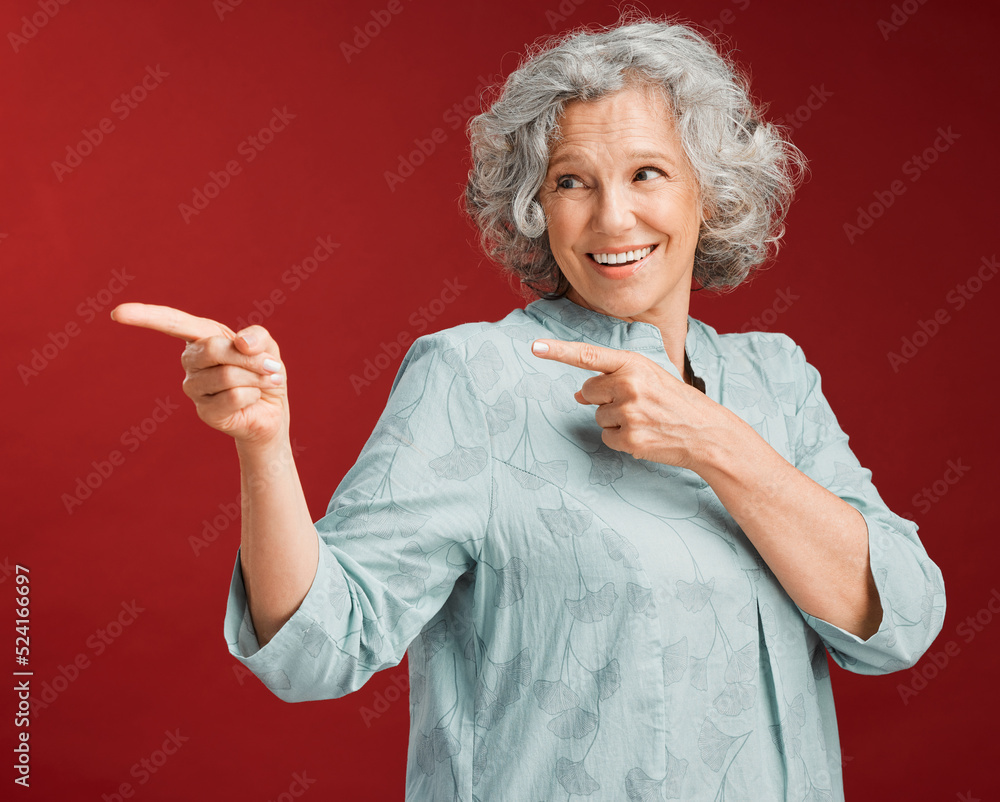 Portrait of mature woman, smiling and pointing with a gesture of affirmation, with a red background.