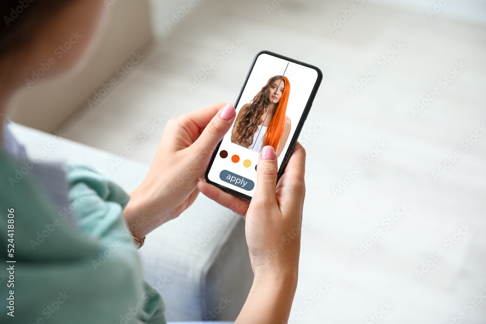 Young woman with modern mobile phone using hair style application at home