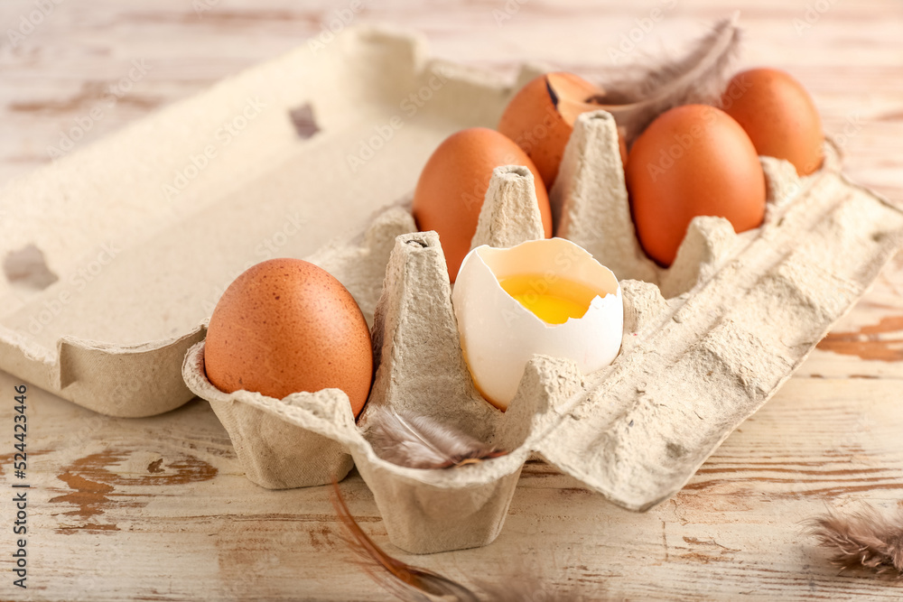 Cardboard holder with chicken eggs on light wooden background, closeup