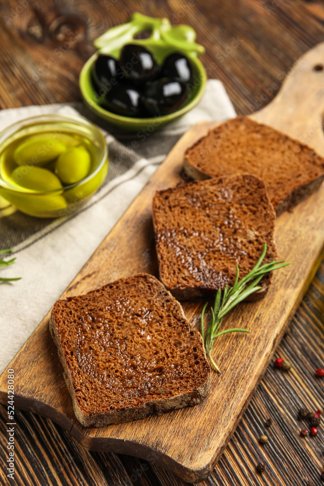 Board with slices of bread and olive oil on wooden table, closeup