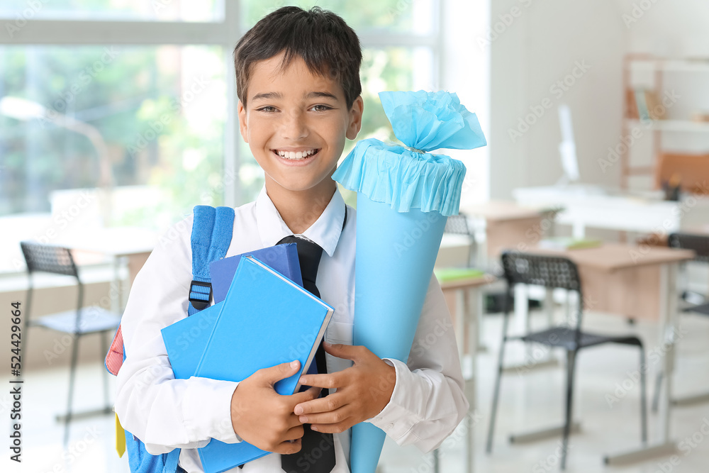 小男孩在教室里拿着蓝色的学校圆锥体和书