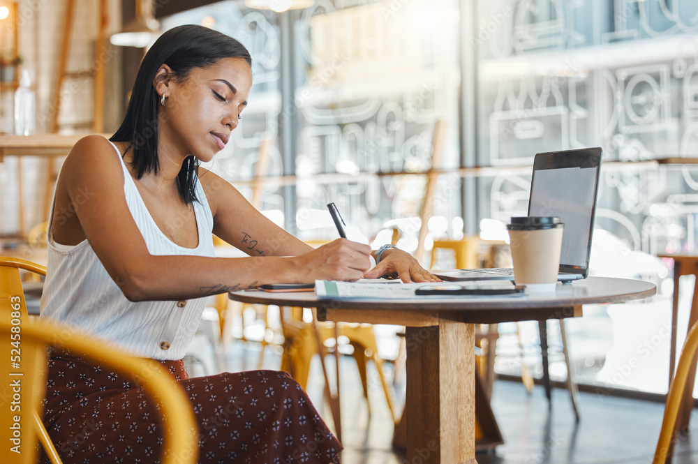 Student writing, taking notes or doing a project assignment in cafe or restaurant using laptop and n