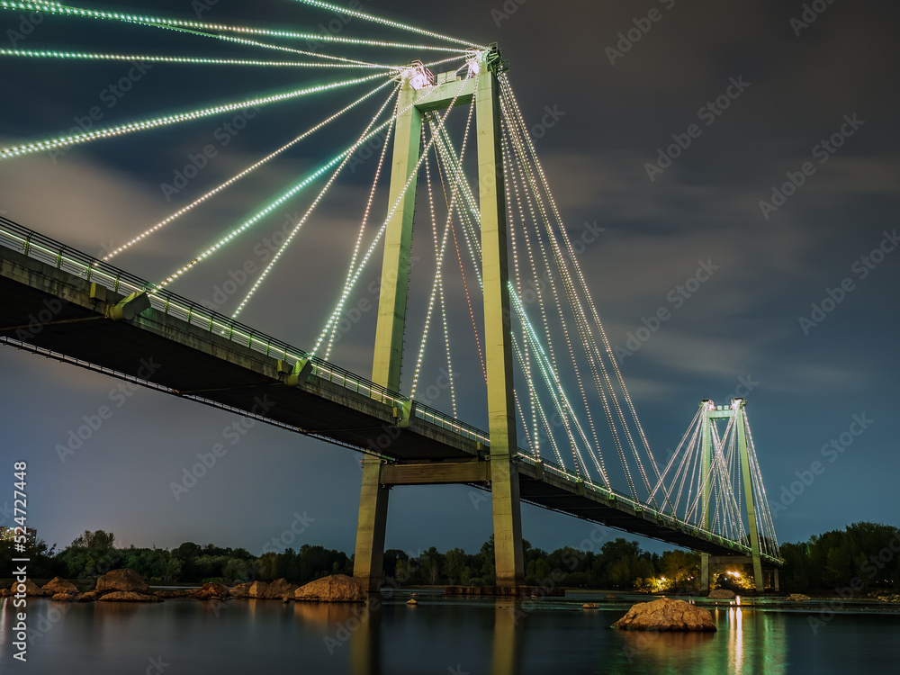 夜间横跨河流的斜拉桥。建筑物的夜间照明，反射。