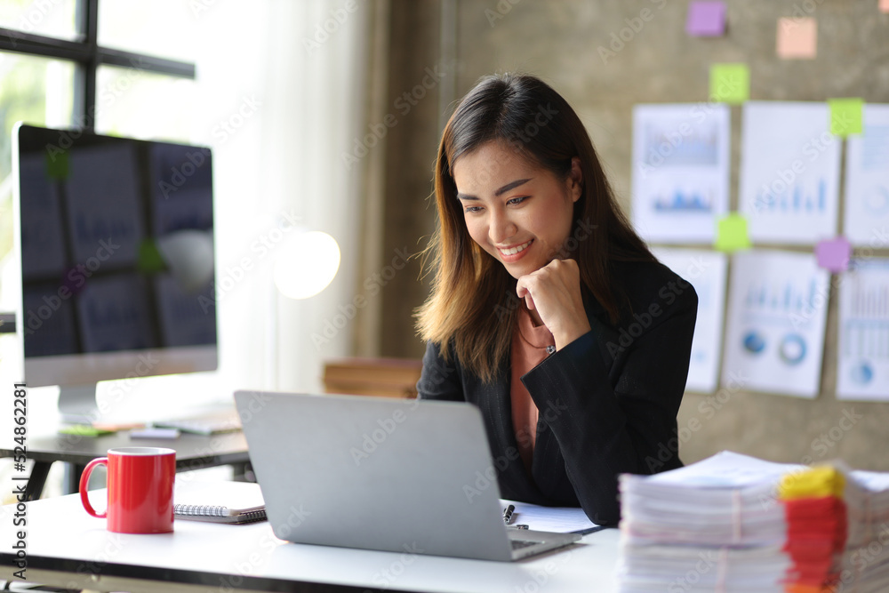 Attractive young Asian business woman in office working on laptop.