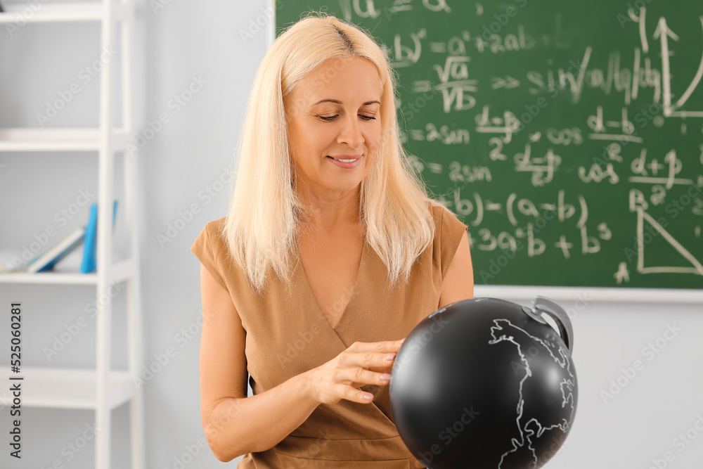 Mature Geography teacher with globe in classroom