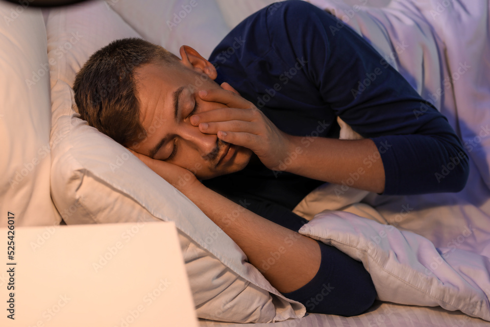 Handsome young man lying in bedroom at night, closeup