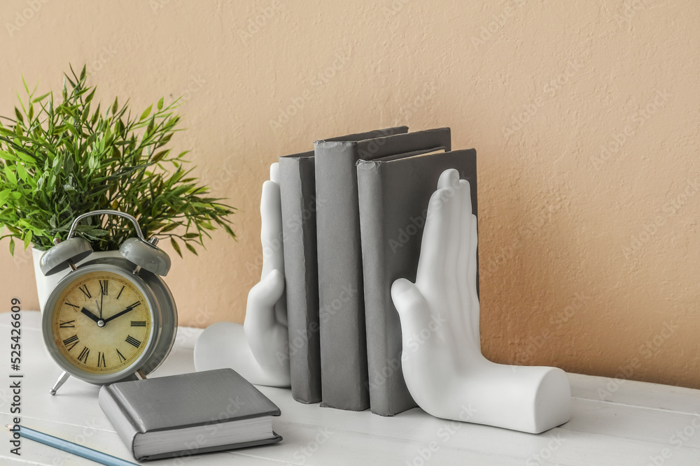 Stylish holder with books and alarm clock on table near beige wall