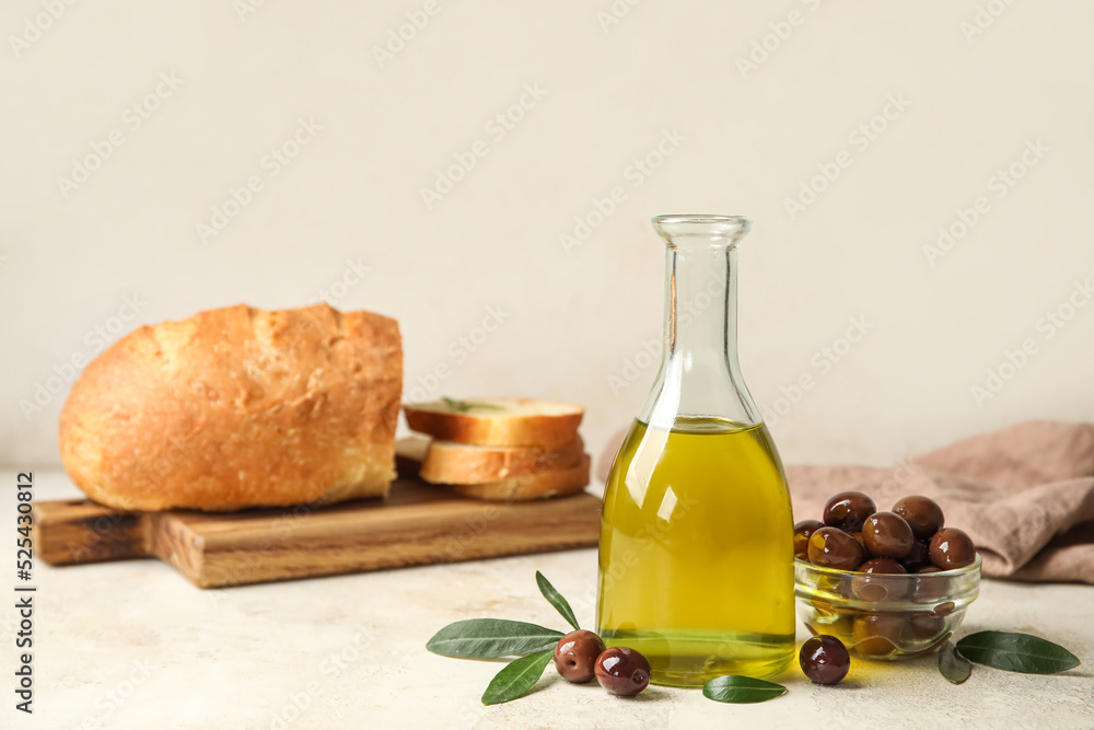 Bottle of fresh oil and bowl with olives on light background