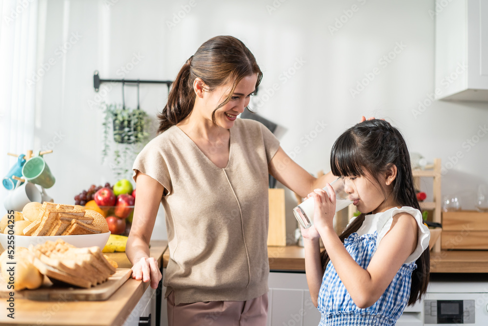 Asian little cute kid holding a cup of milk and drinking with mother