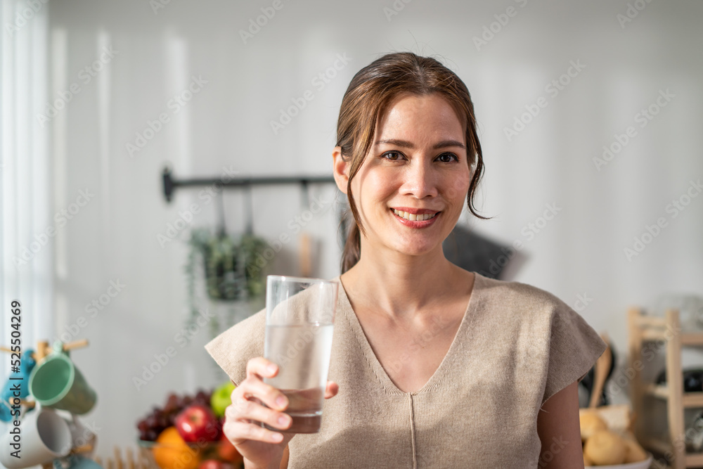 亚洲美女在厨房喝一杯水的肖像。