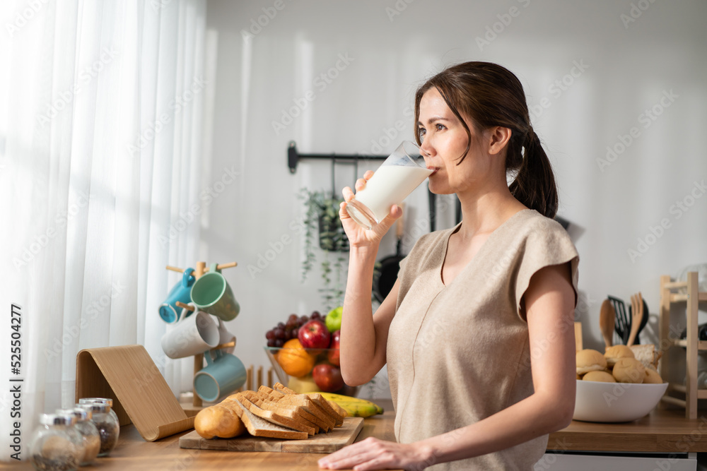 亚洲年轻漂亮女人在家里的厨房里喝着一杯牛奶。