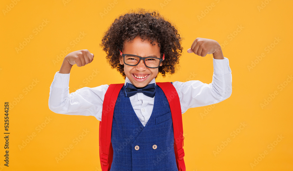 Funny curly schoolboy shows strong muscles on color yellow background