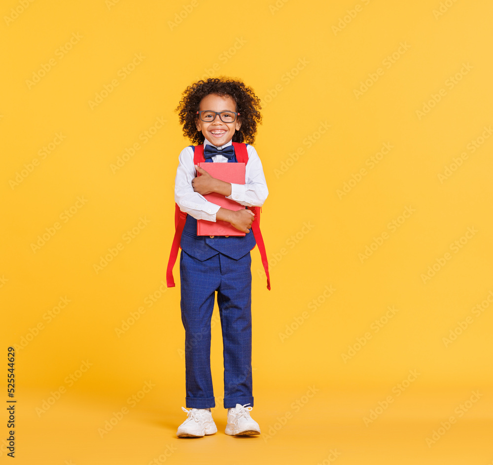 Happy ethnic schoolboy with book laughing