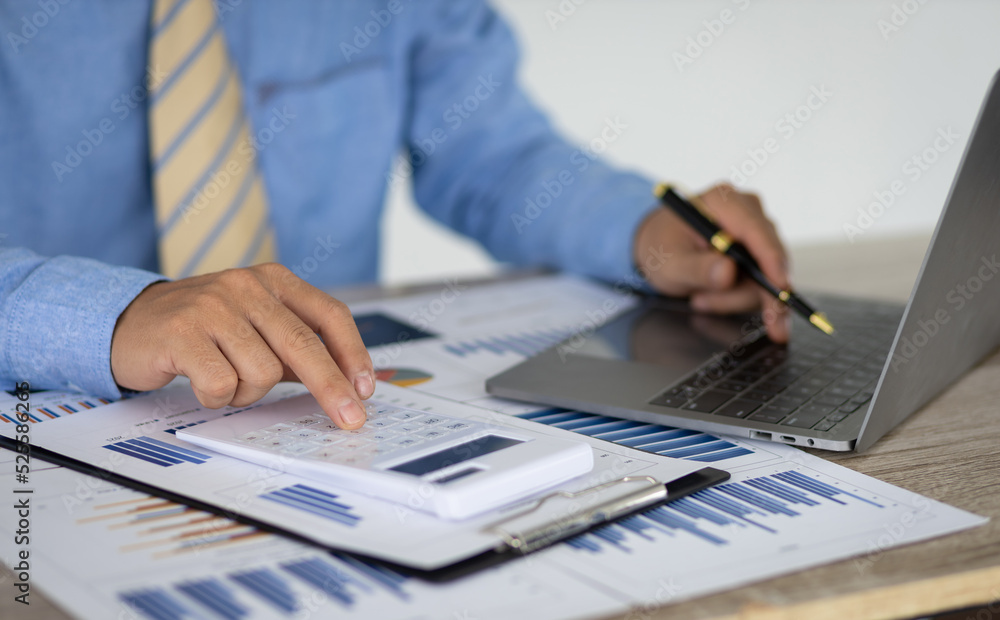 Businessman pointing at chart in document analyzing company sales and financial reports using laptop