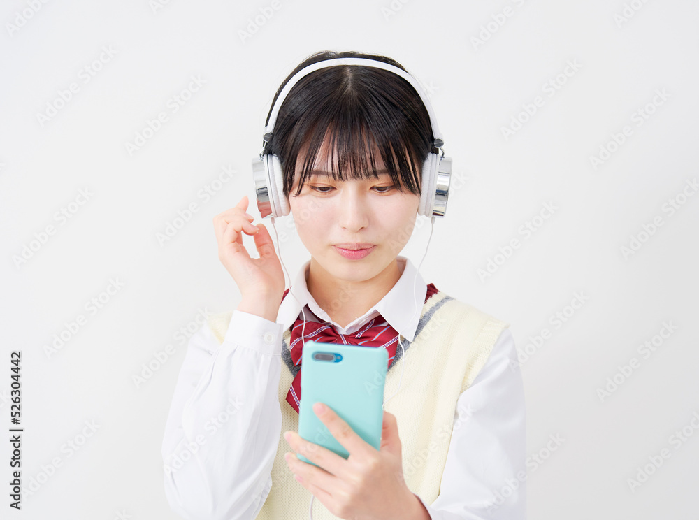 白背景でスマホを持ってヘッドホンで音楽を聴く女子高生