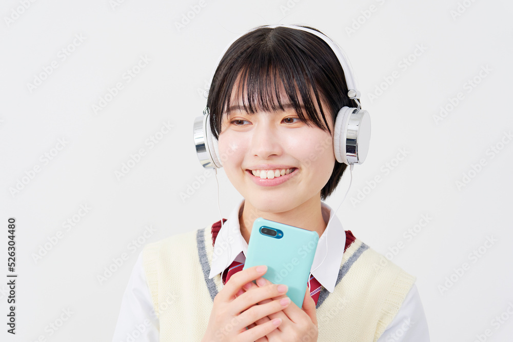 白背景でスマホを持ってヘッドホンで音楽を聴く女子高生