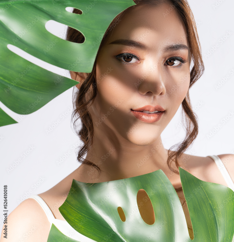 Closeup portrait of young gorgeous woman with healthy fair skin holding big green leaf near her face