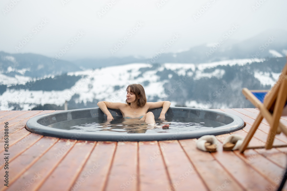 Young woman bathing in hot tub at mountains during winter. Concept of rest and recovery in hot vat o