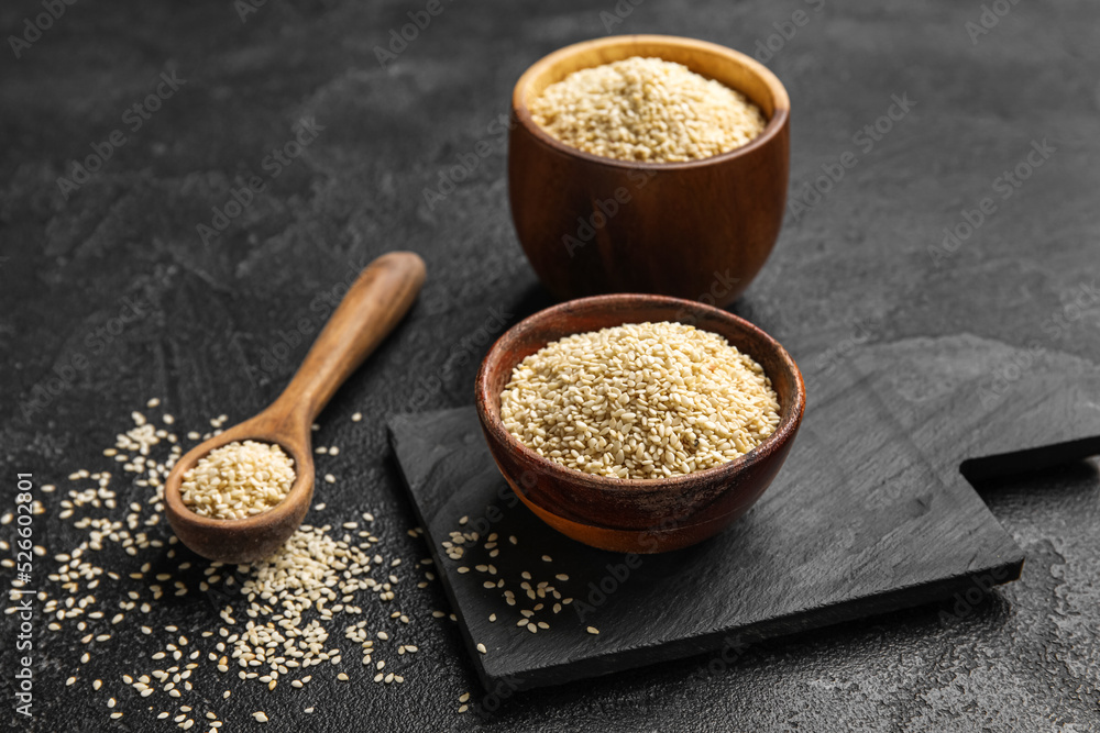 Spoon and bowls of sesame seeds on dark background