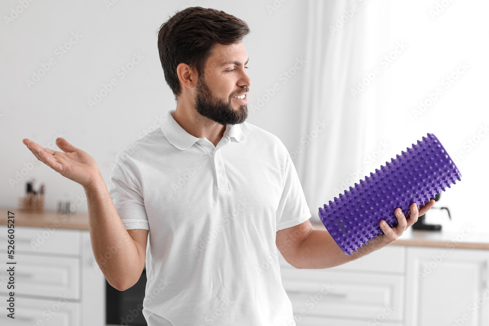 Young man with foam roller in kitchen