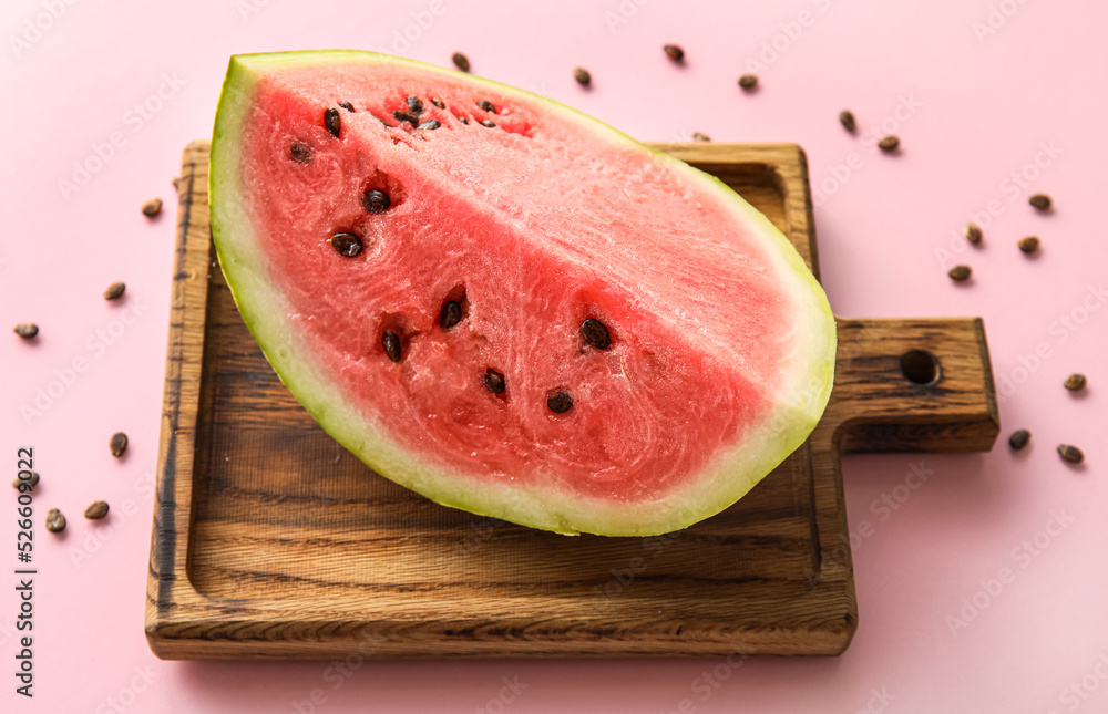 Board with cut watermelon and seeds on pink background