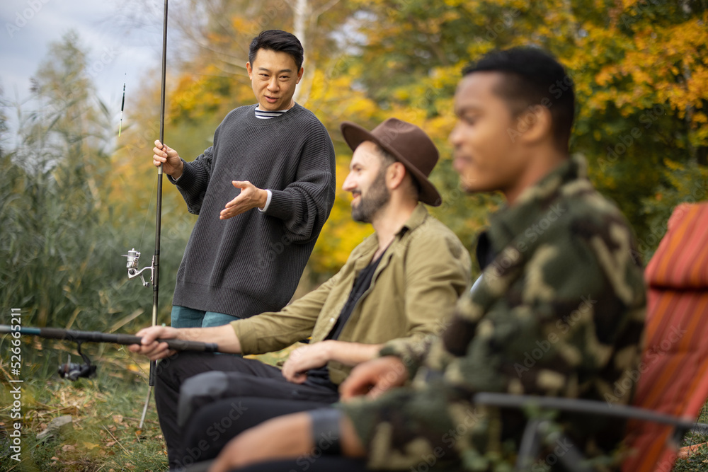 亚洲男人在大自然中钓鱼时与男性多种族朋友交谈。男人休息和消磨时间