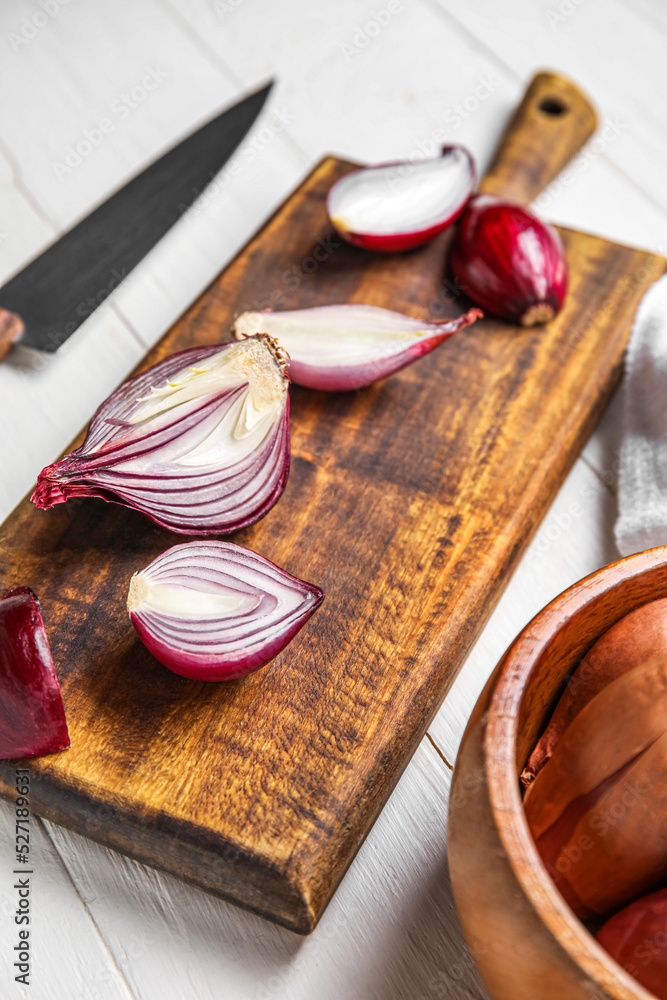 Board with cut red onion on light wooden background, closeup