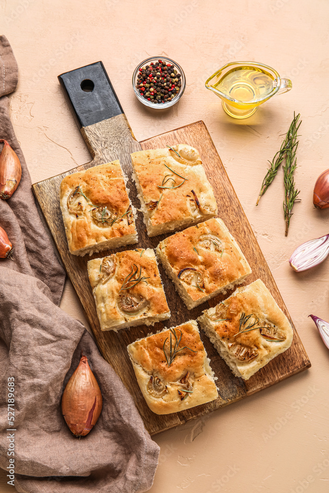 Wooden board with tasty Italian focaccia, onion, oil and peppercorns on color background