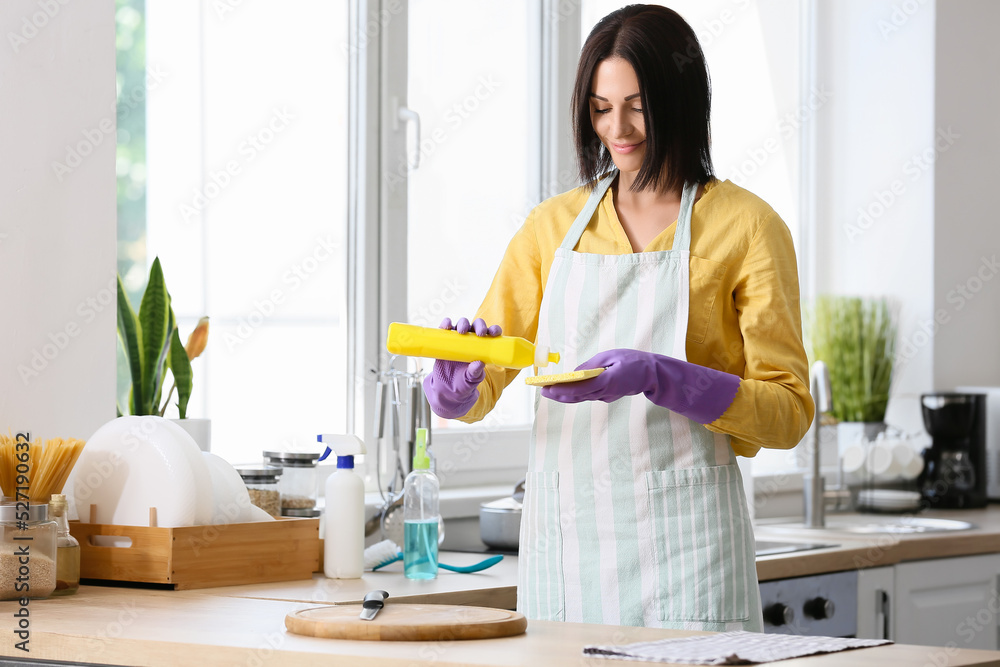 Young woman pouring detergent onto cleaning sponge in kitchen