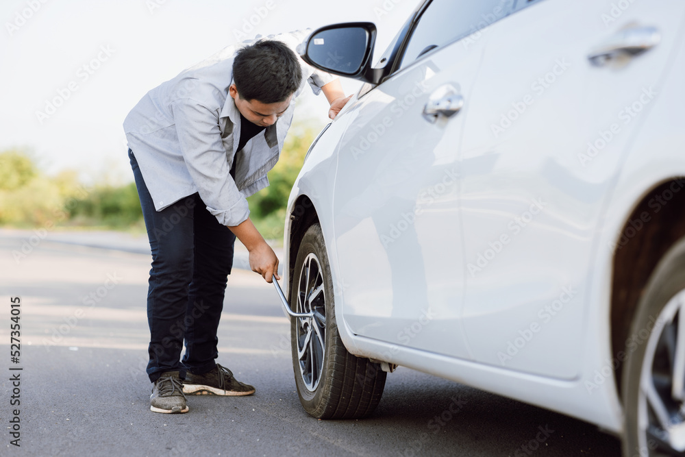 Handsome Asian young man checking wheel flat tire alone on the road.