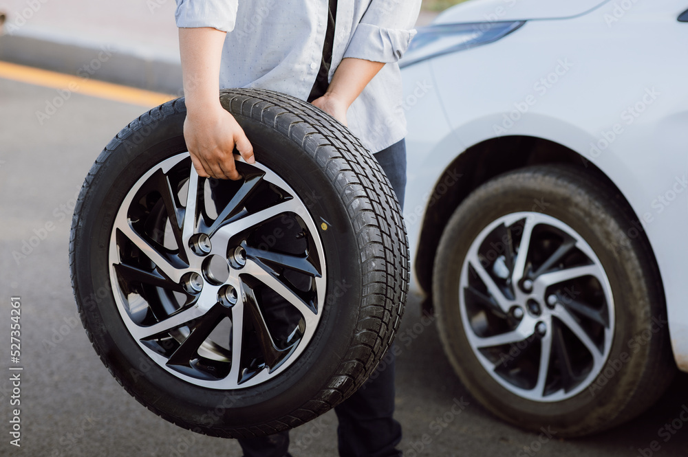 Young man holding spare wheel against for changing flat tire on the road.