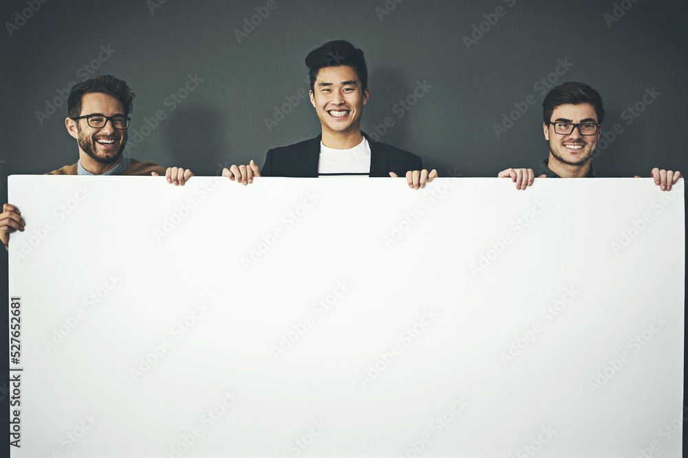 A group of young, smiling and professional business men holding a white sign copyspace portrait. A t