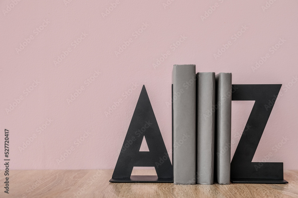 Stylish holder with books on table near pink wall