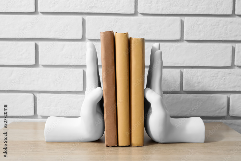 Stylish holder with books on table near white brick wall