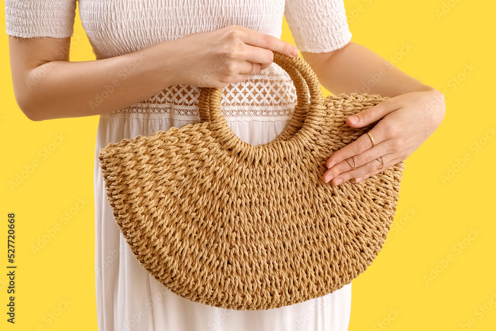 Elegant woman with stylish jewelry holding rattan handbag on yellow background