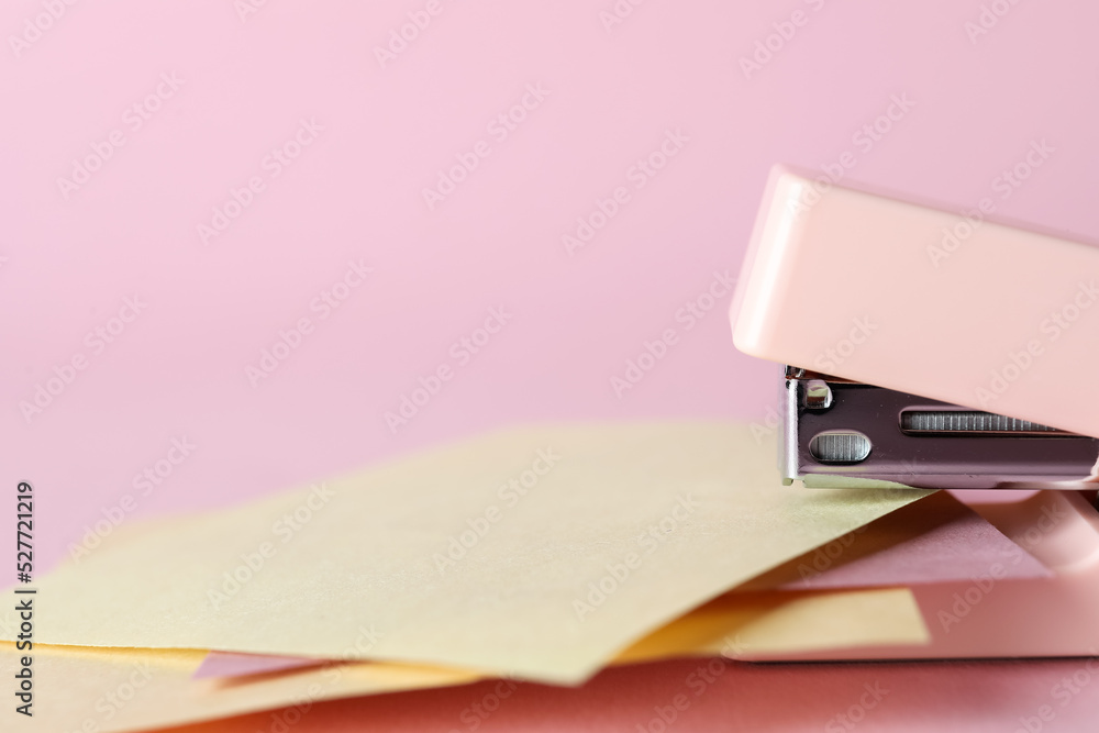 Stapler with sticky notes on pink background, closeup