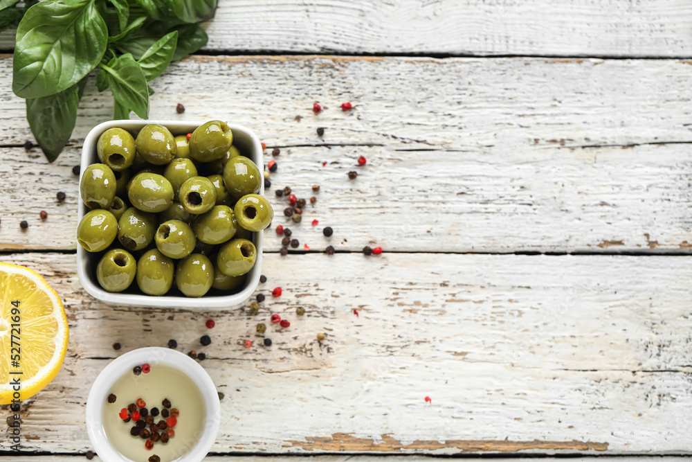 Bowl of green olives, oil and spices on light wooden background