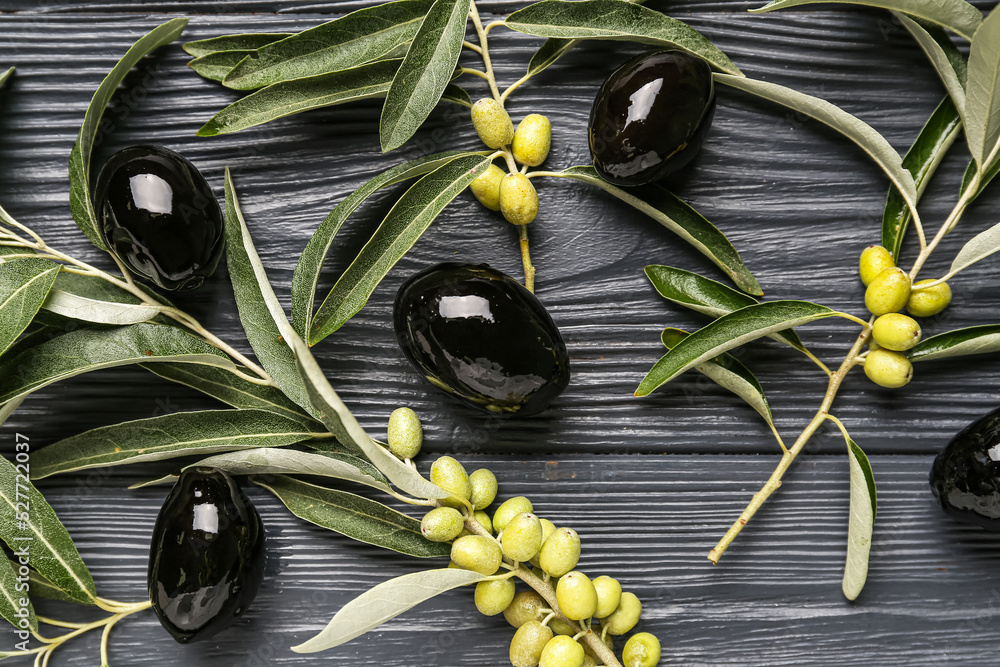 Tasty black olives and tree branches on dark wooden background, closeup