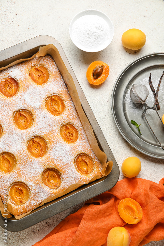 Baking tray with tasty apricot pie and bowl of sugar powder on light background