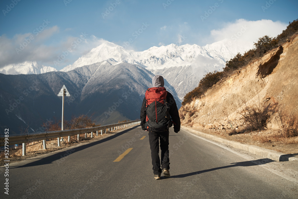 asian hiker backpacker walking on highway with snow mountain in background