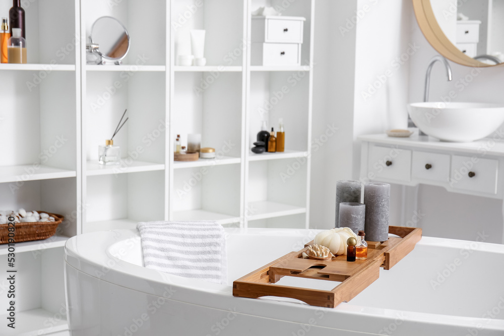 Wooden board with candles, loofah and massage brush in bathroom