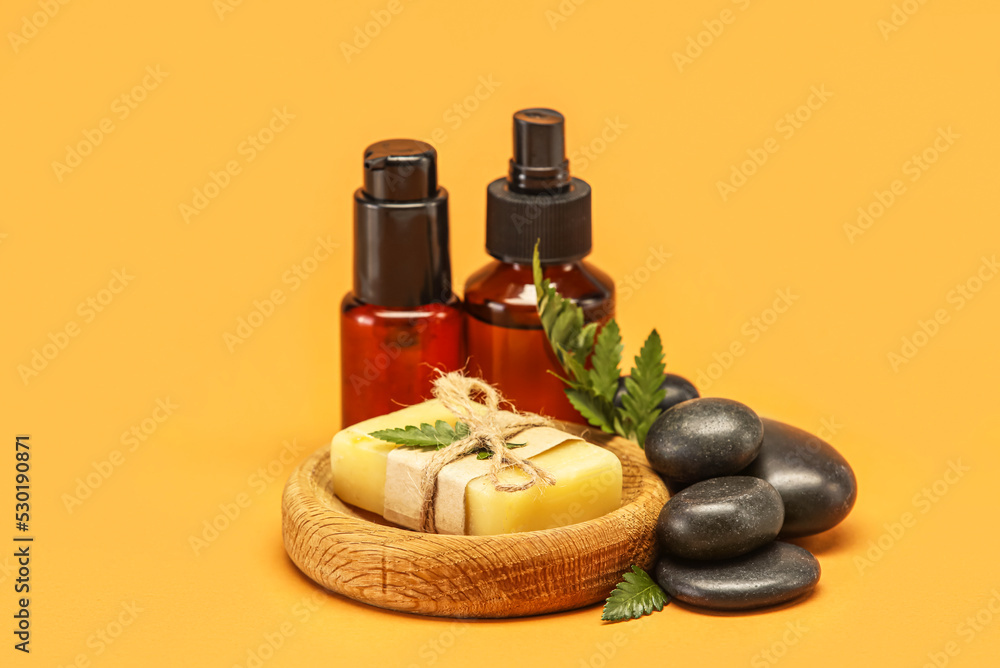 Wooden bowl with soap, spa stones and bottles of cosmetic products on color background