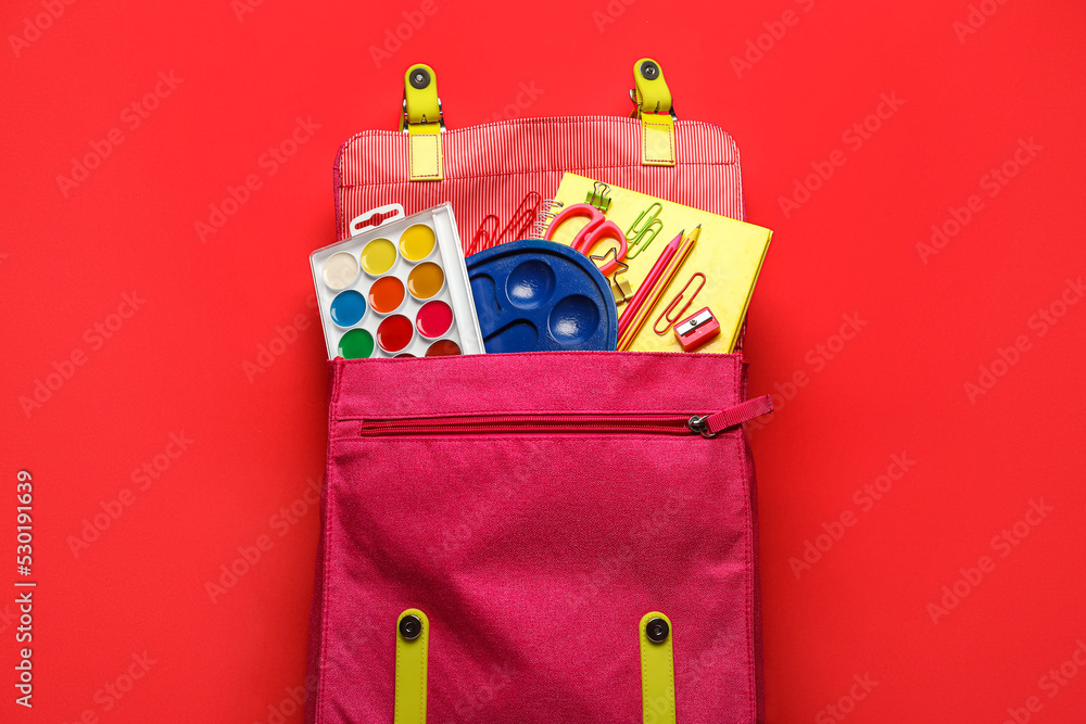 Pink backpack with school stationery on red background