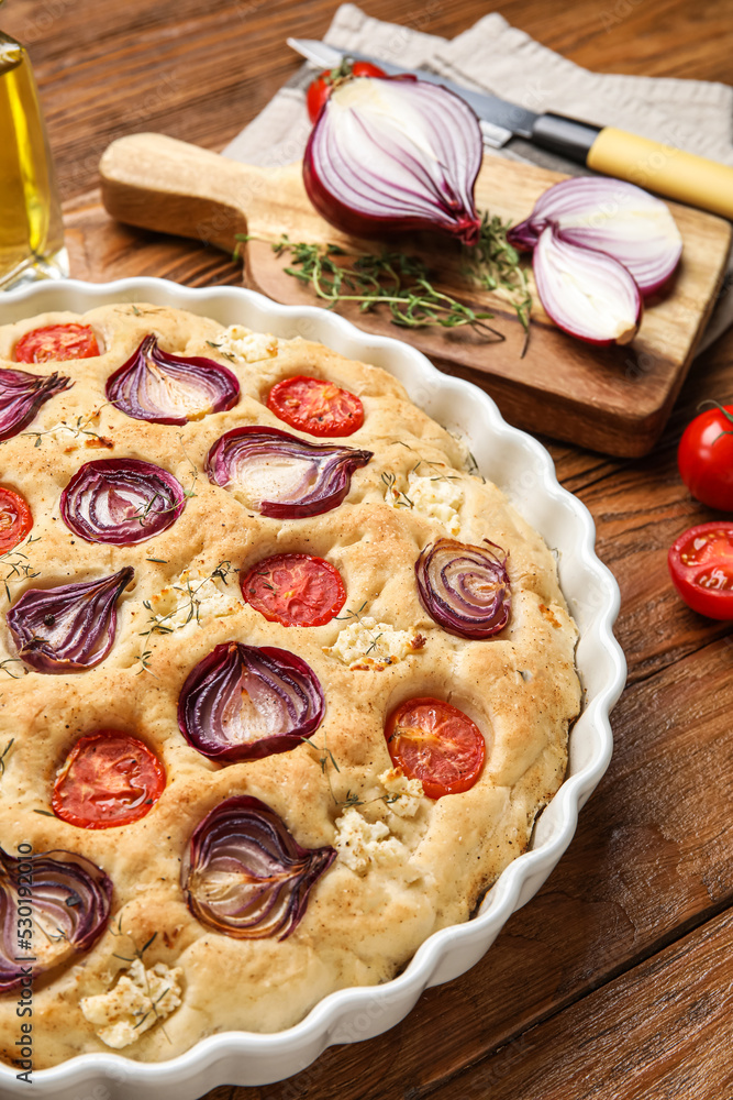 Baking dish of tasty Italian focaccia with vegetables on wooden table, closeup