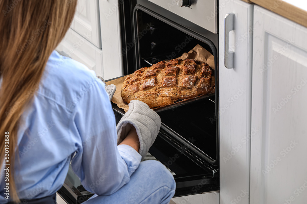 Woman taking baking tray with fresh bread from oven in kitchen, closeup