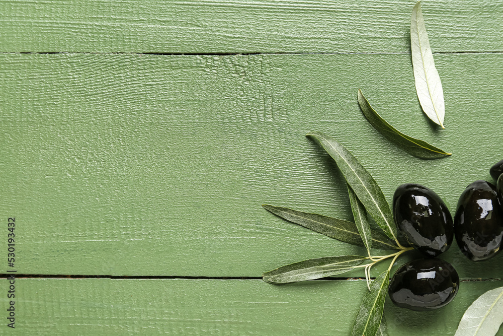 Tasty black olives and leaves on color wooden background