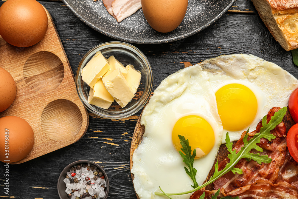 Plate with tasty fried eggs, bacon and butter on dark wooden table, closeup