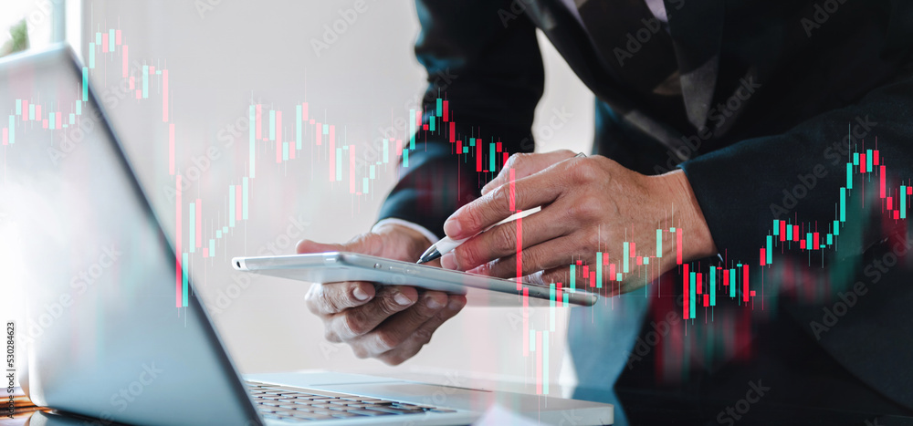 Attractive young european businessman using laptop with abstract forex chart. Investment and economy